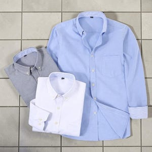 Puede incluir: Tres camisas abotonadas en azul claro, blanco y gris. La camisa azul claro está desabrochada, revelando el interior. La camisa blanca está doblada y la camisa gris está plana. Todas las camisas tienen cuellos abotonados y mangas largas.