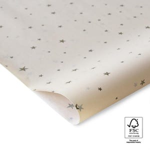 Könnte beinhalten: Cremefarbenes Geschenkpapier mit einem sich wiederholenden Muster aus kleinen, grauen Sternen. Das Papier ist teilweise gerollt und zeigt seine Unterseite. Das FSC-Logo ist sichtbar, was verantwortungsvolle Forstwirtschaft anzeigt.