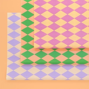 Könnte beinhalten: Drei Blätter gemustertes Papier in einem Stapel. Das oberste Blatt hat ein rosa-gelbes Rautenmuster. Das mittlere Blatt hat ein grün-pfirsichfarbenes Rautenmuster. Das untere Blatt hat ein lila-cremefarbenes Rautenmuster.