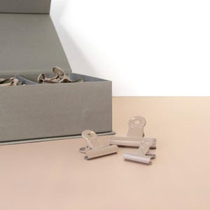 Könnte beinhalten: Ein Set aus drei Keramikbechern mit gesprenkelter, matter Oberfläche. Die Becher sind in Creme-, Hellgrau- und Dunkelgrautönen gehalten. Jeder Becher hat ein schlichtes, minimalistisches Design.