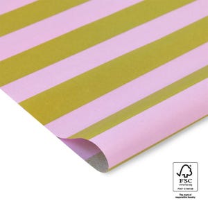 Könnte beinhalten: Rosa-gold gestreiftes Geschenkpapier. Das Papier hat breite, diagonale Streifen in einem sanften Rosa und einem gedämpften Goldton. Eine Ecke des Papiers ist umgefaltet, wodurch die Unterseite sichtbar wird. Das FSC-Logo befindet sich unten rechts.