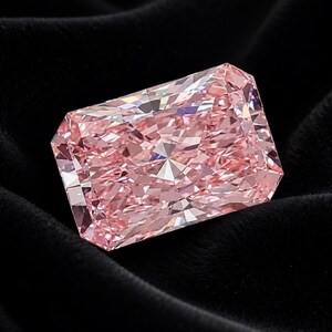 Op de afbeelding: Een rechthoekige edelsteen met een radiant-slijpvorm, een zachtroze tint en talloze facetten die een schitterend, reflecterend oppervlak cre&euml;ren. De steen heeft een heldere, kristallijne structuur met scherpe randen en een geometrische vorm.