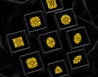Op de afbeelding: Een verzameling van negen levendige gele edelstenen, elk afzonderlijk gepresenteerd in een klein, vierkant zwart doosje. De stenen hebben verschillende slijpvormen, waaronder smaragd, rond, princess, ovaal, marquise en driehoekige vormen.