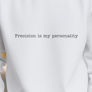 Puede incluir: Sudadera blanca de cuello redondo con el texto "Precision is my personality" en negro. La sudadera es de color blanco liso y tiene un diseño sencillo y clásico.