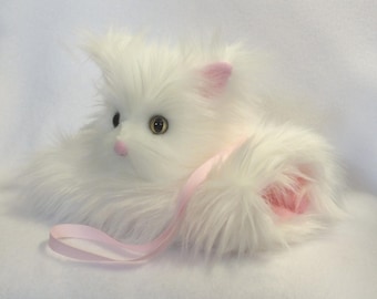 May include: A plush white cat with long, fluffy fur, pink inner ears, and a pink nose. The cat has large, round eyes and a pink ribbon. The toy cat is lying down on a white surface.