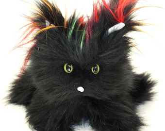 May include: A black plush toy cat with green eyes and colorful, spiky hair. The toy has a white nose and ears. The cat is sitting down and has a fluffy appearance.