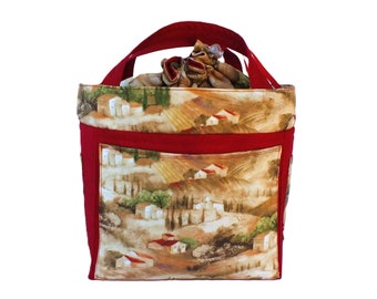 May include: Red and brown tote bag with a landscape design featuring houses and trees. The bag has a red handle and a red trim around the top.