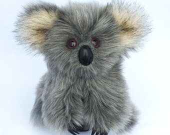 May include: A gray and brown plush koala bear with black eyes and a black nose. The koala is sitting with its paws in front of it.