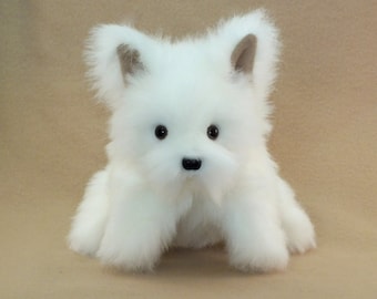 May include: A white plush toy dog with brown ears and black eyes. The dog is sitting on a brown surface.