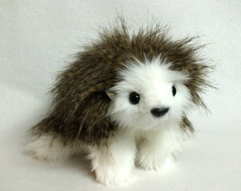 May include: A plush toy hedgehog with brown and white fur. The hedgehog has a white face with black eyes and a black nose.