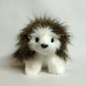 May include: A white and brown plush toy hedgehog with black eyes and a black nose. The hedgehog has a fluffy, spiky coat.