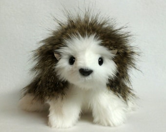 May include: A white and brown plush toy hedgehog with black eyes and a black nose. The hedgehog has a fluffy, spiky coat.