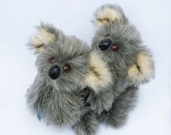 May include: Two gray plush koala bears with black eyes and noses. The koala bears are hugging each other.