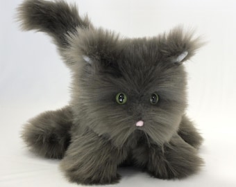 May include: A plush gray cat toy with green eyes and a pink nose. The cat has a fluffy, textured appearance, with its tail curved upwards. The toy is designed to resemble a cat and is likely intended for children or cat lovers.