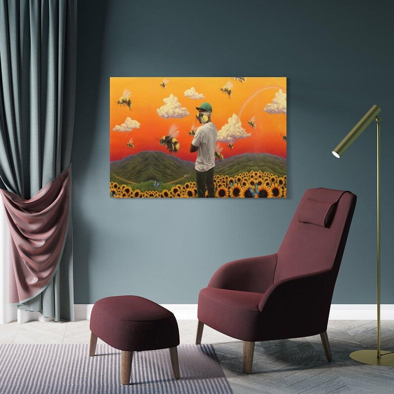 May include: A framed art print depicts a person in a field of sunflowers, surrounded by bees, under a sunset sky. The artwork is displayed above a burgundy armchair and ottoman, with a gold floor lamp and blue wall.