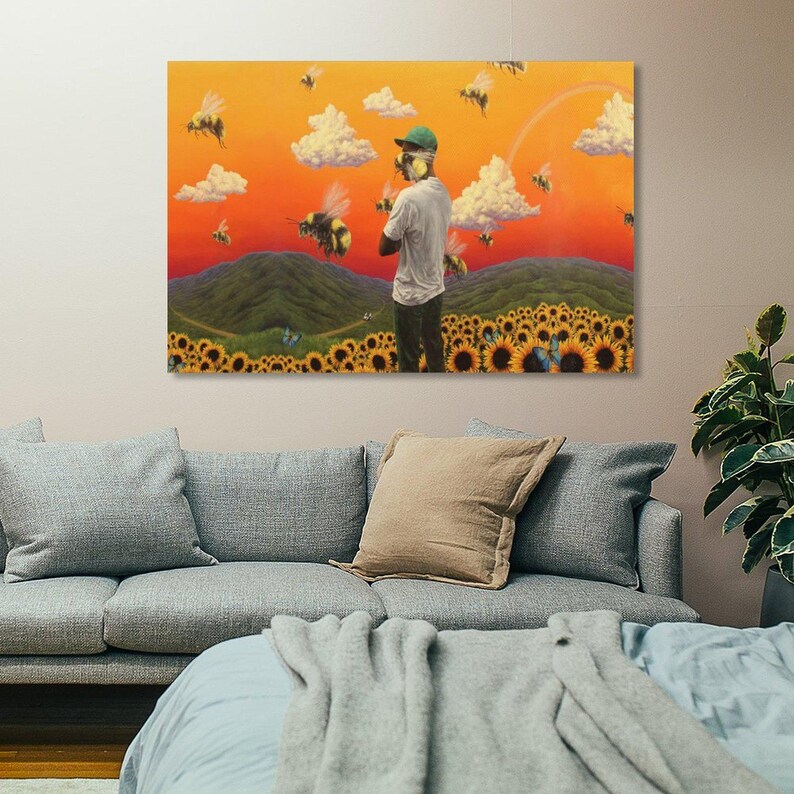 May include: A canvas print featuring a surreal landscape with a person standing in a field of sunflowers. The artwork depicts a vibrant orange sky, fluffy white clouds, and several bees. The person is wearing a green cap and a white shirt.