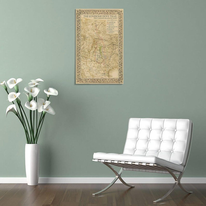 Puede incluir: Un mapa vintage enmarcado titulado "The Lonesome Dove Trail" con un borde decorativo. El mapa est&aacute; en tonos beige y marr&oacute;n, montado en una pared verde claro. Una silla blanca moderna y un jarr&oacute;n con flores blancas est&aacute;n en primer plano.