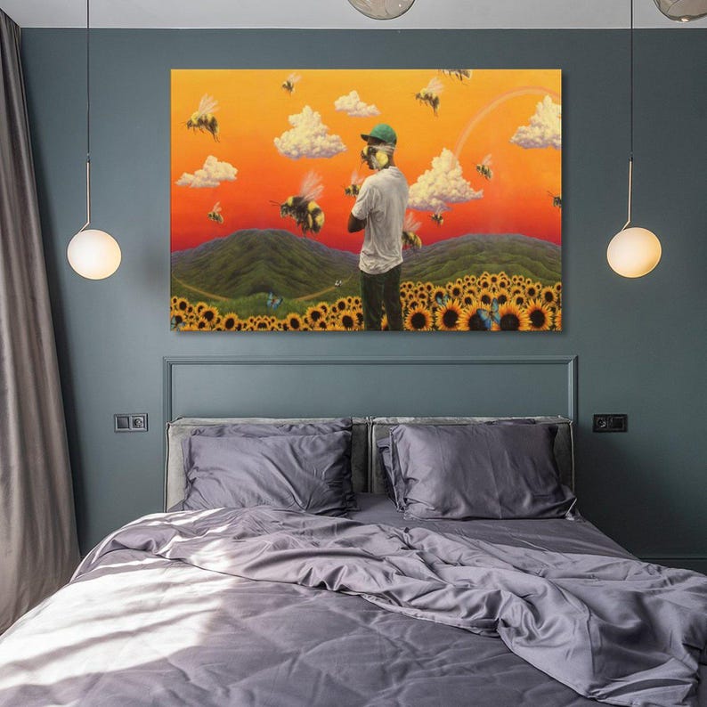 May include: A large, framed canvas art print depicting a surreal landscape with a person standing in a field of sunflowers, surrounded by bees. The background features rolling green hills, fluffy clouds, and an orange and yellow sky.