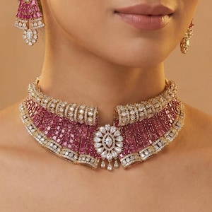 Może przedstawiać: Luksusowy zestaw biżuterii z naszyjnikiem i pasującymi kolczykami z rubinami i diamentami. Naszyjnik jest w stylu choker, z centralnym motywem kwiatowym i kaskadą kamieni w kolorze rubinu. Kolczyki odzwierciedlają wzór naszyjnika.