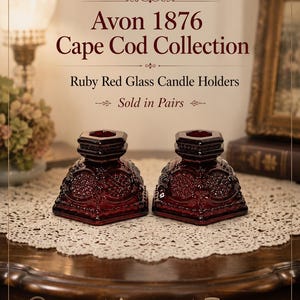 May include: A pair of ruby red glass candle holders from the Avon 1876 Cape Cod Collection. These pressed glass candle holders feature a hexagonal base and a textured geometric pattern on the sides, with a central opening for a taper candle.