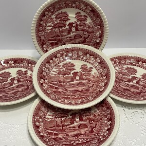 May include: A set of five ceramic plates with a red and white landscape design. The plates have a scalloped edge and a detailed illustration of a bridge, trees, and buildings. The plates are arranged in a stack.
