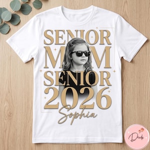 May include: White t-shirt featuring a black and white photo of a young girl wearing sunglasses. The shirt has the words "SENIOR MOM SENIOR 2026 Sophia" in gold lettering, with star accents. A personalized graduation gift.