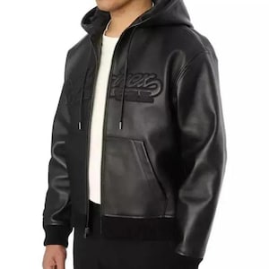 Pu&ograve; includere: Giacca con cappuccio nera con zip e tasca frontale. La giacca presenta la scritta "Rex" ricamata sul petto. La giacca ha orlo e polsini a coste. Il modello indossa una maglietta bianca sotto.