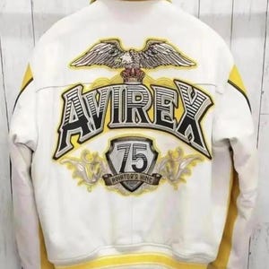 May include: White leather jacket with yellow accents and the text "AVIREX" and "75 AVIATOR'S KING" on the back. Features an eagle graphic above the text. The jacket has a yellow collar and stripes.
