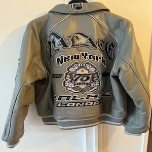 May include: A gray leather jacket with a white and black design on the back. The jacket has a collar and a ribbed hem. The back of the jacket features the words "PALACE New York" and "AVIREX 75 PALACE LONDON".