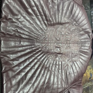 May include: A burgundy leather jacket with a quilted design. The back of the jacket features an embroidered emblem with the text "GOLD KICKS" in a stylized font. The jacket has a classic, tailored fit.