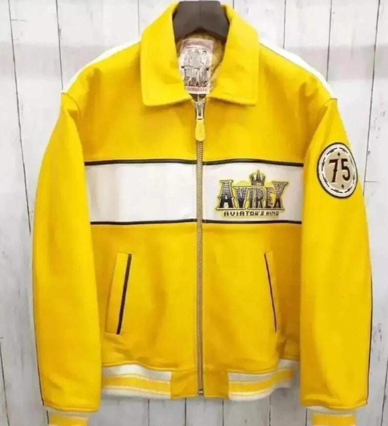 May include: Yellow jacket with a white stripe across the chest and sleeves. The jacket has a zipper closure and a collar. The brand name "AVIREX" is displayed on the chest, and a patch with the number "75" is on the sleeve.