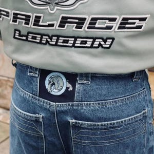 May include: Close-up of a light gray jacket with the text "PALACE LONDON" in black and white. Below, blue denim jeans with a patch featuring a bulldog graphic are visible.