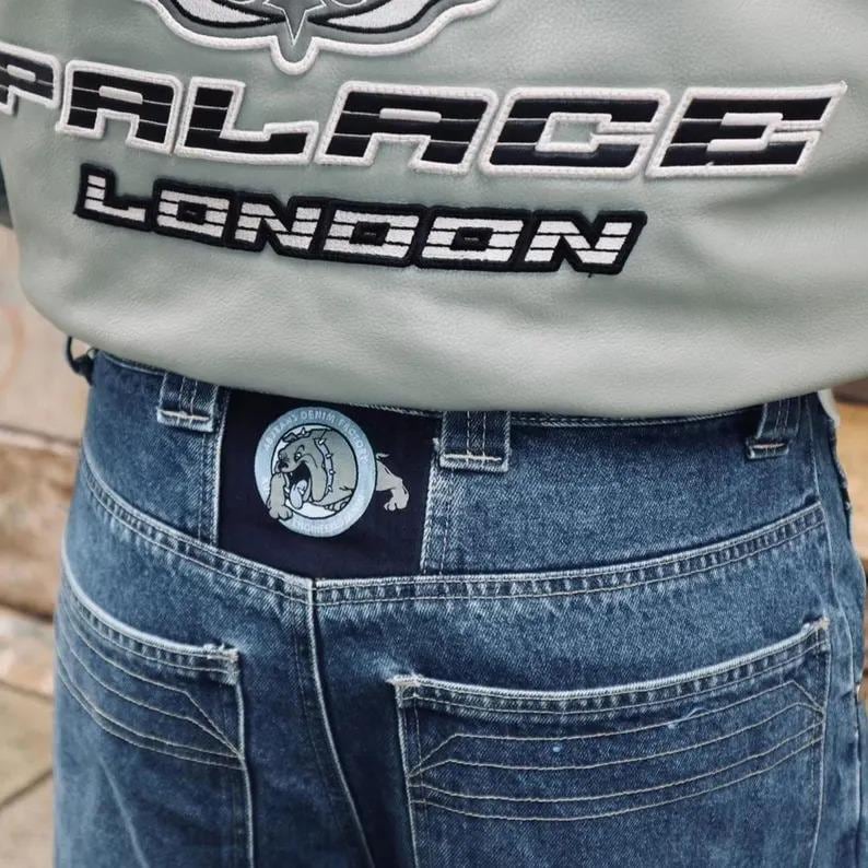 May include: Close-up of a light gray jacket with the text "PALACE LONDON" in black and white. Below, blue denim jeans with a patch featuring a bulldog graphic are visible.