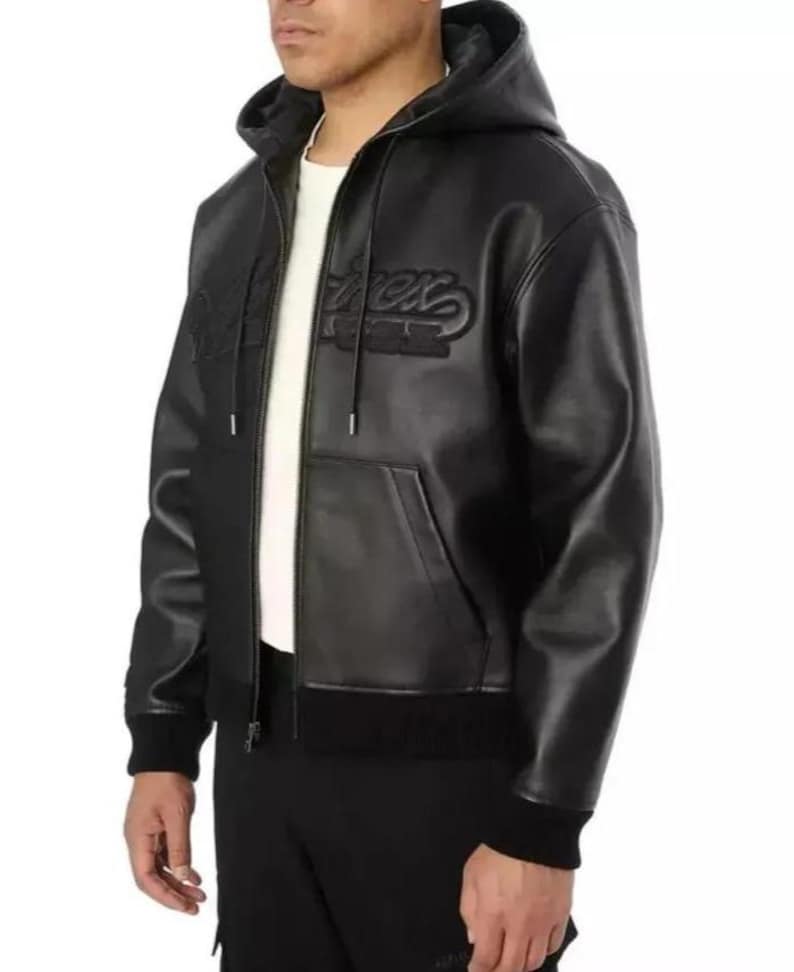 Pu&ograve; includere: Giacca con cappuccio nera con zip e tasca frontale. La giacca presenta la scritta "Rex" ricamata sul petto. La giacca ha orlo e polsini a coste. Il modello indossa una maglietta bianca sotto.