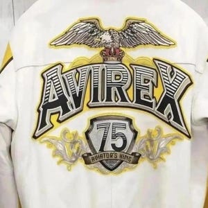 May include: White jacket with yellow accents and the word "AVIREX" in large, black and yellow lettering. The back of the jacket features an eagle emblem above the text and a "75" patch with "AVIATOR'S KING" text.