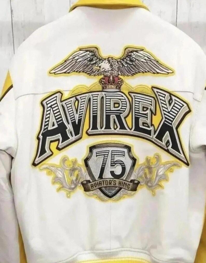 May include: White jacket with yellow accents and the word "AVIREX" in large, black and yellow lettering. The back of the jacket features an eagle emblem above the text and a "75" patch with "AVIATOR'S KING" text.