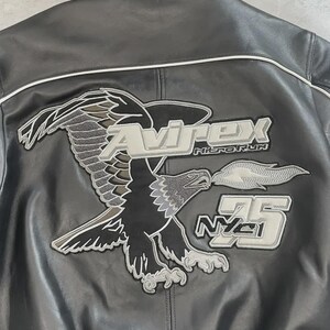 May include: Black leather jacket featuring an embroidered eagle motif on the back. The design includes the text "Avirex Nitro Run" and "75 NYC". The jacket has white piping along the seams.