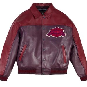 Puede incluir: Chaqueta de cuero burdeos y morado con cierre de botones, cuello y pu&ntilde;os y dobladillo acanalados. La chaqueta presenta un parche en el pecho con la palabra "AVIREX" en un dise&ntilde;o estilizado. Dos bolsillos delanteros.