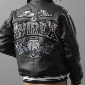 May include: Black leather jacket with white and black striped cuffs and hem. The back features a large embroidered design with the word "AVIREX", a soaring eagle, and the number "75" within a shield.