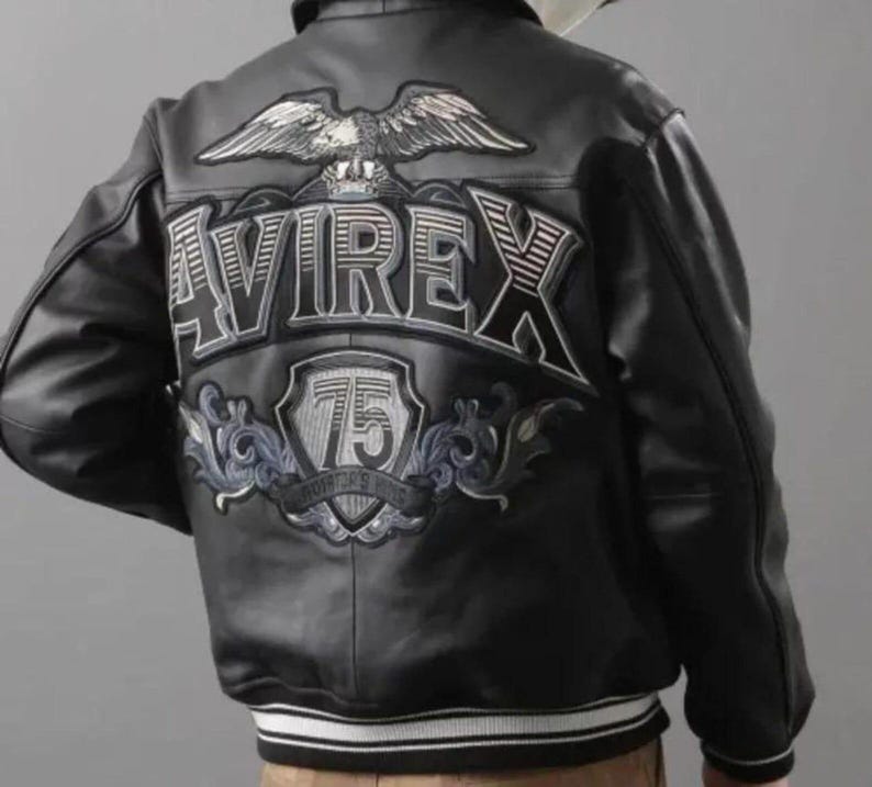 May include: Black leather jacket with white and black striped cuffs and hem. The back features a large embroidered design with the word "AVIREX", a soaring eagle, and the number "75" within a shield.
