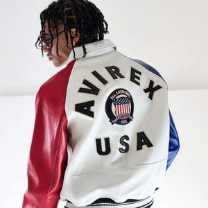 May include: White, red, and blue leather jacket with the text "AVIREX" and "USA" on the back. The jacket features a patch with the words "ALL AMERICANS" and the American flag. The sleeves are red and blue.