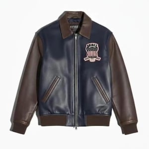 May include: A navy blue leather jacket with brown sleeves and collar. The jacket features a zipper closure and a patch on the chest with the text "AVIREX" and a patriotic design. The jacket has a ribbed hem and cuffs.
