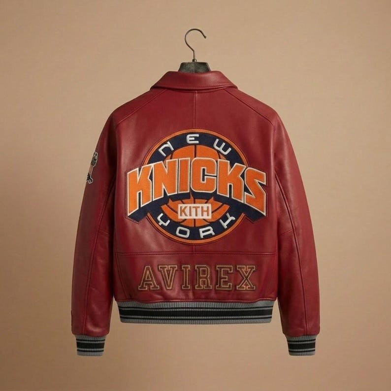 Puede incluir: Una chaqueta universitaria de cuero rojo con un gran parche circular en la espalda con el texto NEW YORK KNICKS y KITH en naranja y azul marino. La palabra AVIREX est&aacute; bordada en dorado debajo del parche. La chaqueta tiene pu&ntilde;os acanalados.