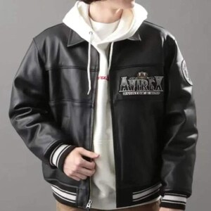 May include: Black leather jacket with a white hooded sweatshirt underneath. The jacket features a collar, a zipper closure, and striped cuffs and hem. The jacket has the text "AVIREX" on the chest.