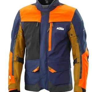 May include: A multi-colored motorcycle jacket with orange, navy blue, black, and tan panels. The jacket has multiple pockets, zippers, and the KTM logo on the chest. The jacket has a high collar and is designed for protection and style.