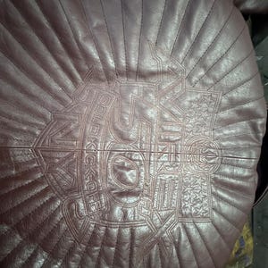 May include: A burgundy leather jacket with a quilted design. The back of the jacket features an embroidered emblem with the words "SOLDIER KICKOFF" and star details. The stitching creates a sunburst pattern.