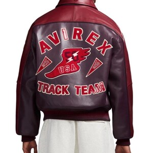 Puede incluir: Chaqueta de cuero burdeos con cuello y mangas en rojo oscuro en contraste. La espalda presenta el texto "AVIREX TRACK TEAM" en blanco, con un emblema de EE. UU. rojo y blanco. La chaqueta tiene dobladillo y pu&ntilde;os acanalados.