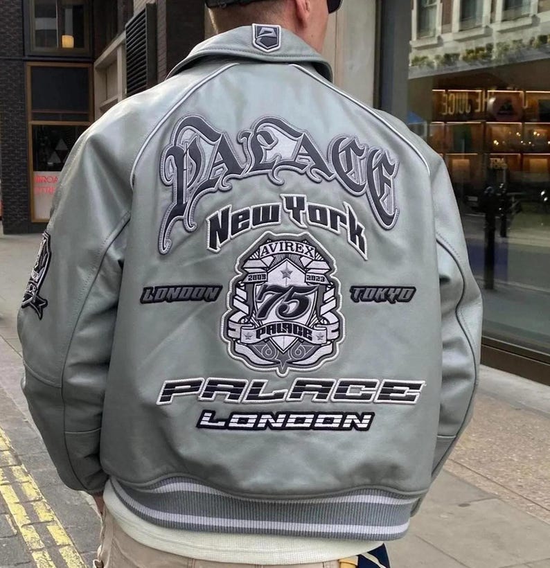 May include: A light grey leather jacket with the word "PALACE" in large, stylized lettering across the back, along with "New York", "London", and "Tokyo". The jacket features a patch commemorating "75 Palace Pride" and the Avirex brand.