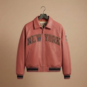 Puede incluir: Una chaqueta tipo bomber de color rosa empolvado con cremallera frontal completa, cuello cl&aacute;sico y pu&ntilde;os y dobladillo acanalados con rayas negras. El texto NEW YORK est&aacute; bordado en el pecho en letras oscuras con un acabado de textura sutil.