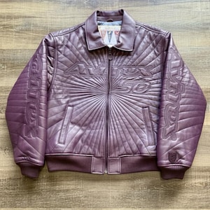 May include: A purple leather jacket with a quilted design and a zip-up front. The jacket features the text "AVIREX 50" across the chest and on the sleeves. It has a collared neckline and ribbed cuffs and hem.